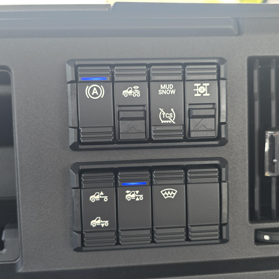 Dashboard switches in a Mack AN64T showing traction/auxiliary controls with icons for parking brake, mud/snow, stability, tow/haul, and defogger indicators.