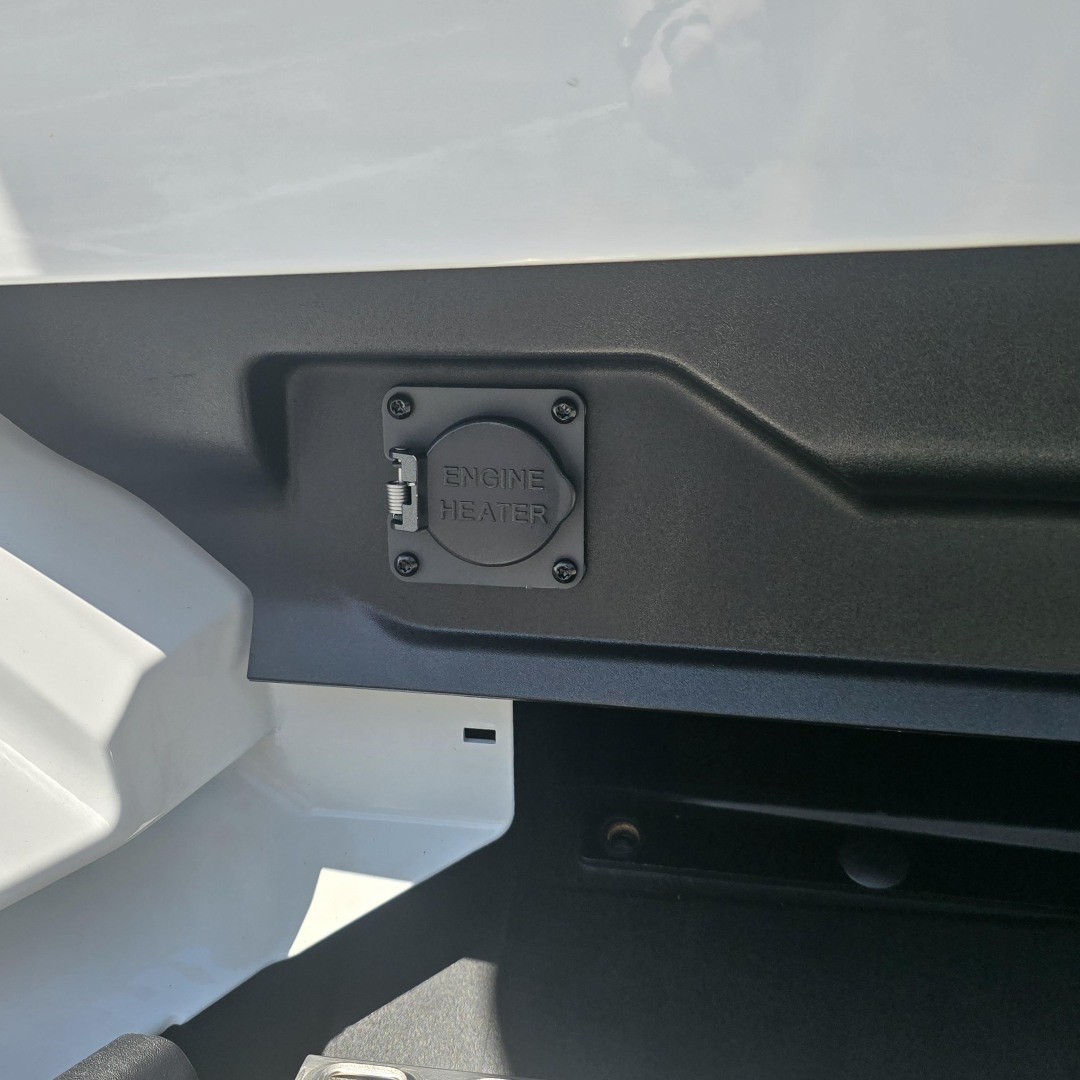 Truck cab area showing engine heater inlet cap with four screws on a panel.