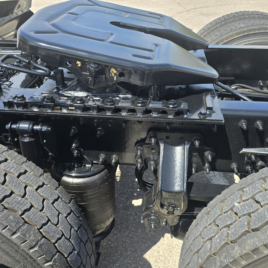 Mack AN64T cab chassis showing engine bay area with suspension and air filter canister visible, view of front wheel and frame members.