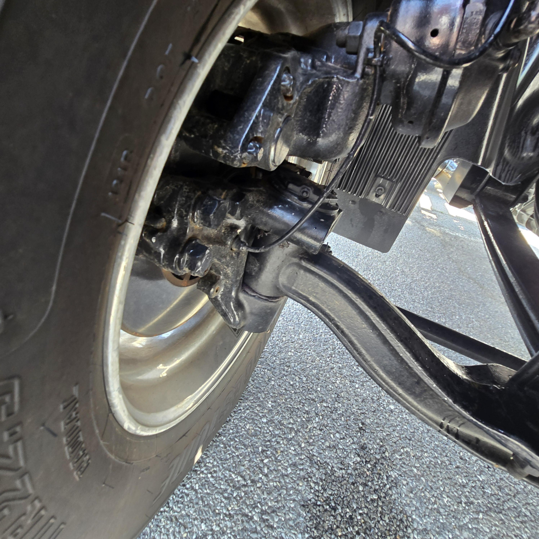 Front axle and suspension of a Mack AN64T truck showing wheel, leaf spring, and drivetrain components.