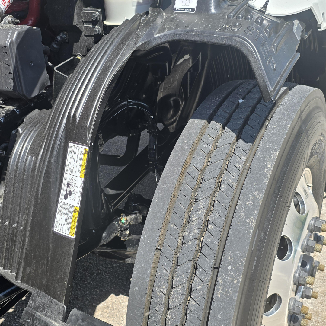 Truck front left wheel and fender area showing front axle and tire; visible labels on black fender guard and nearby components.