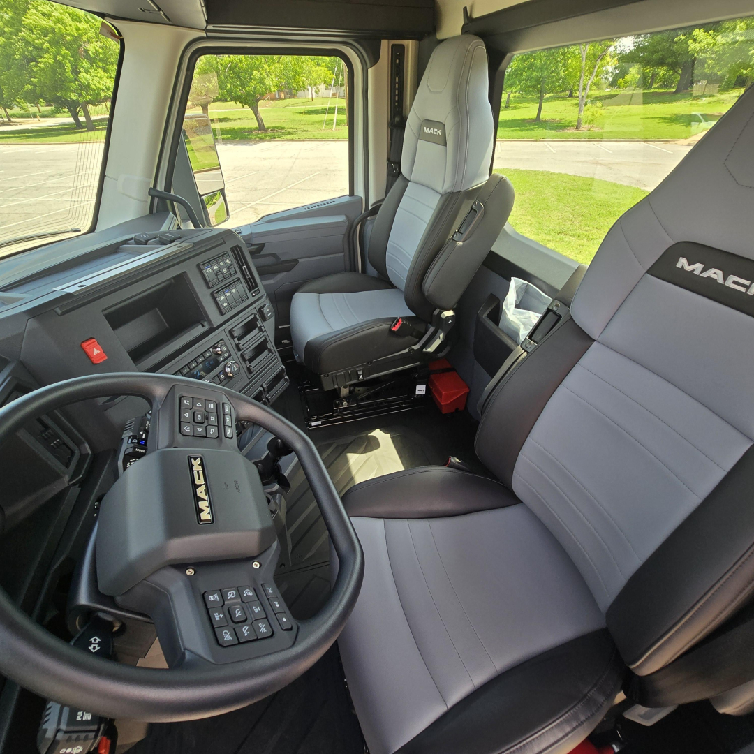 Cab interior of a 2027 Mack AN64T truck showing steering wheel with Mac brand, grey and black seats, dashboard, and spacious cabin.