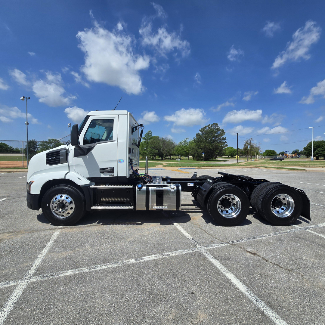 Truck side view of a white 2027 Mack AN64T conventional daycab with tandem rear axles in an empty parking lot.