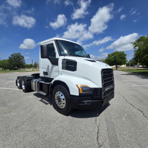 White 2027 Mack AN64T conventional daycab truck profile view in parking lot with blue sky and clouds.