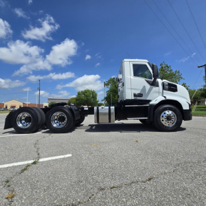 Truck chassis and cab of a 2027 Mack AN64T on concrete lot, side view showing front tires, cab, and rear axle.