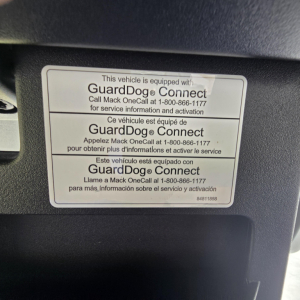 Sticker showing GuardDog Connect device label on Mack AN64T truck, with multilingual text and phone number for Mack OneCall service activation.