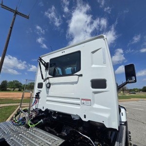 Mack AN64T truck cab in white, side view showing door, windshield wipers, mirrors, and exposed wiring harnesses on the lower front of the cab.