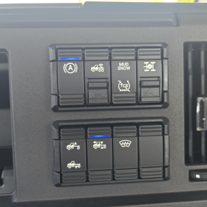 Dashboard switches in a Mack AN64T showing traction/auxiliary controls with icons for parking brake, mud/snow, stability, tow/haul, and defogger indicators.