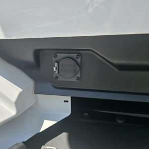 Truck cab area showing engine heater inlet cap with four screws on a panel.