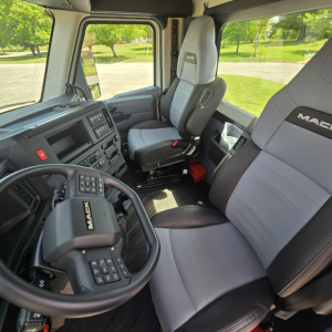 Cab interior of a 2027 Mack AN64T truck showing steering wheel with Mac brand, grey and black seats, dashboard, and spacious cabin.