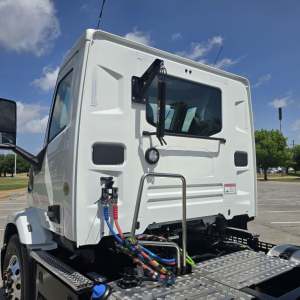 Truck cab rear view showing multi-colored hydraulic lines and chassis connection.