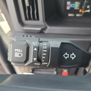 Truck steering column stalks with turn signal lever and headlight control in a Mack AN64T cab. Visible labels include PULL for headlights and HI/LO OFF settings, and left/right indicator icon.