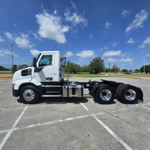 Truck side view of a white 2027 Mack AN64T conventional daycab with tandem rear axles in an empty parking lot.