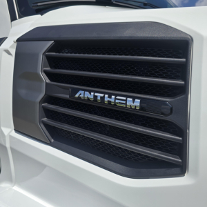 Front grille of a white Mack truck showing the ANTHEM badge in the center with black mesh and horizontal slats.