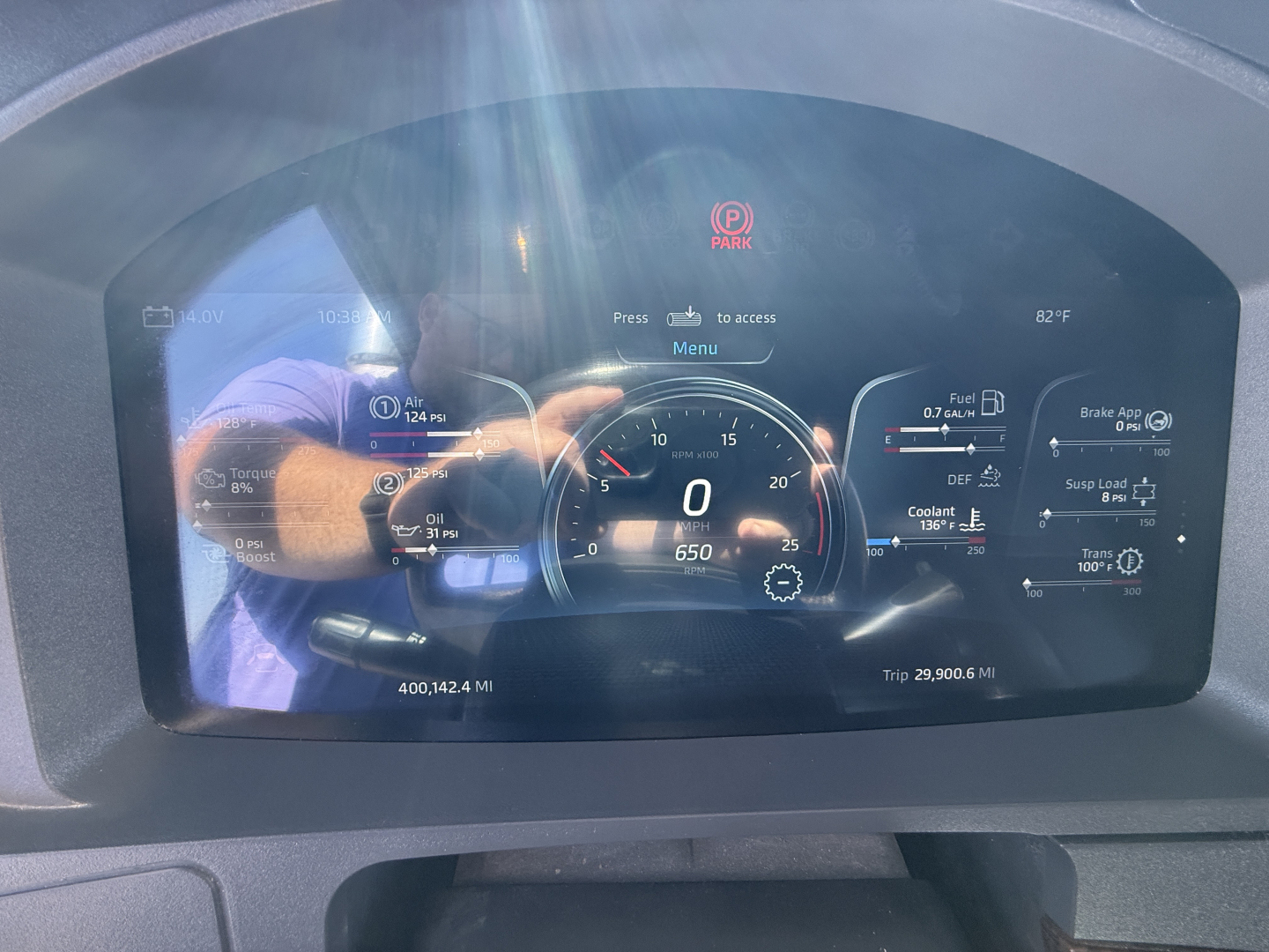 Kenworth W990 instrument cluster showing digital speedometer at 0 mph, trip meters, and various gauges; center display with Park indicator and 0.0 miles; reflection of person taking photo.