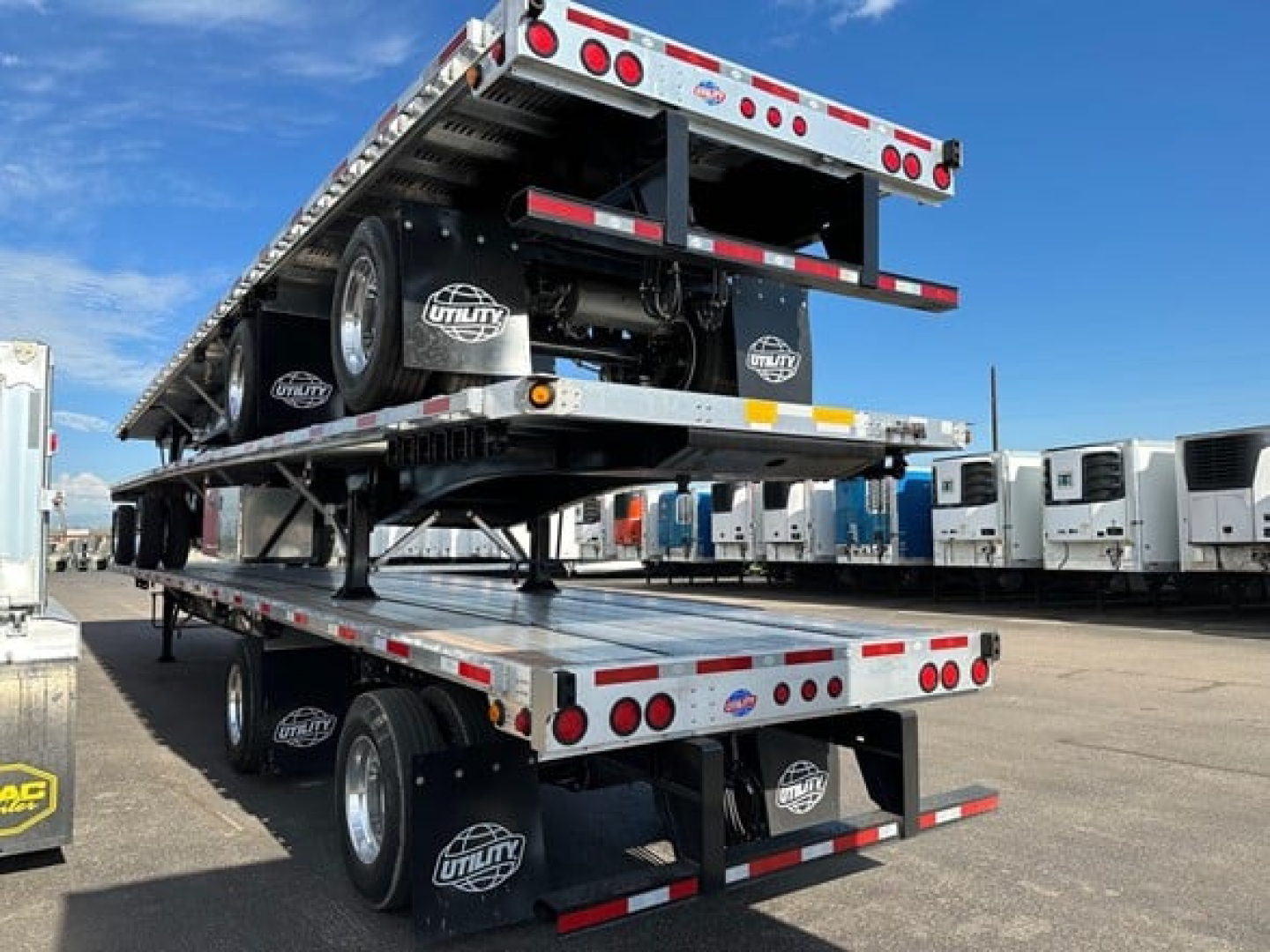 Flatbed trailer stack showing multiple aluminum flatbed decks and dual rear axles. Visible logos on mudflaps and wheels, with a second deck lifted above the first.