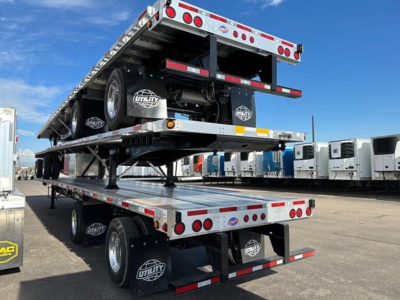 Flatbed trailer stack showing multiple aluminum flatbed decks and dual rear axles. Visible logos on mudflaps and wheels, with a second deck lifted above the first.