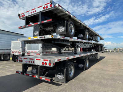 Utility 4000Ae flatbed trailer stacked with two levels of trailers on a service lot, dual rear axles, chrome fuel tanks, and branded mud flaps.