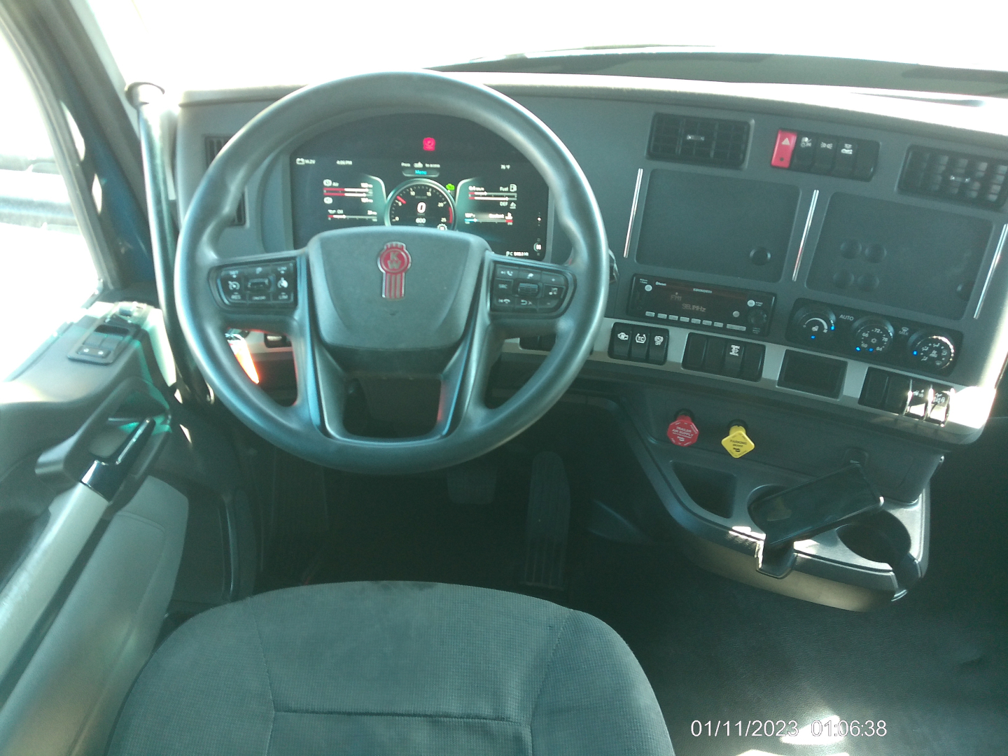 Kenworth T680 cabin dashboard and steering wheel with digital gauges and center console controls.