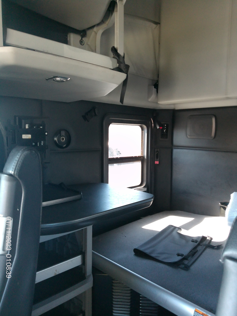 Kenworth T680 cab interior showing sleeper area with bunk bed and table, side windows, and overhead storage.