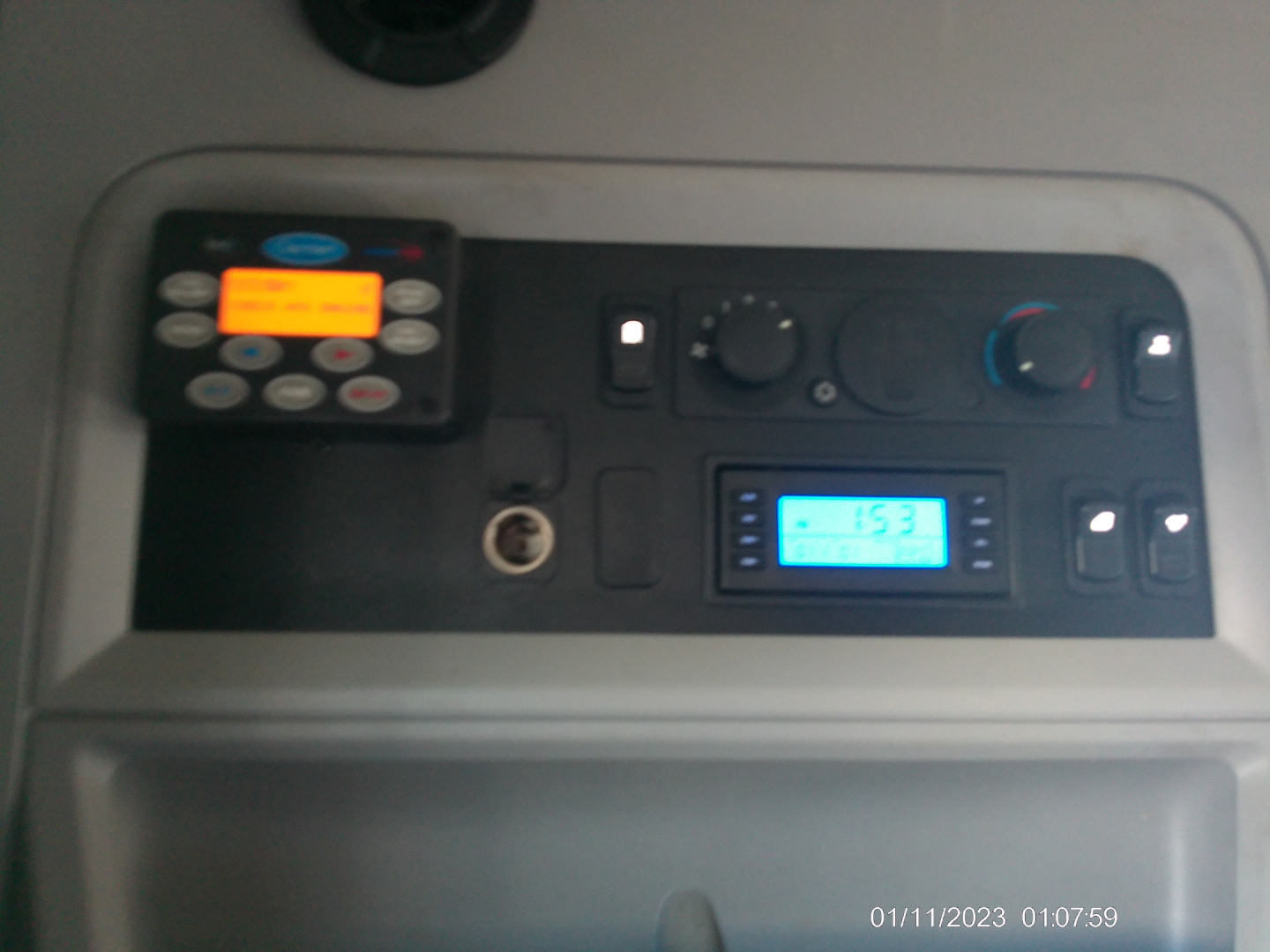 Kennworth T680 dashboard view showing control panel with keypad, small orange display, blue-lit LCD screen, and circular knobs.