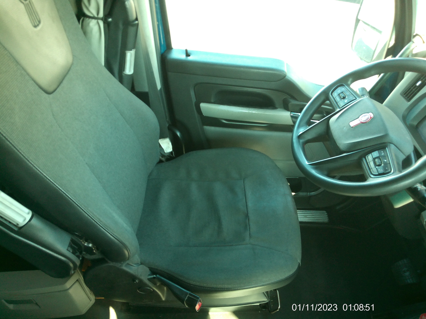 Truck cab interior showing driver seat and steering wheel of a Kenworth T680, with steering wheel badge visible.