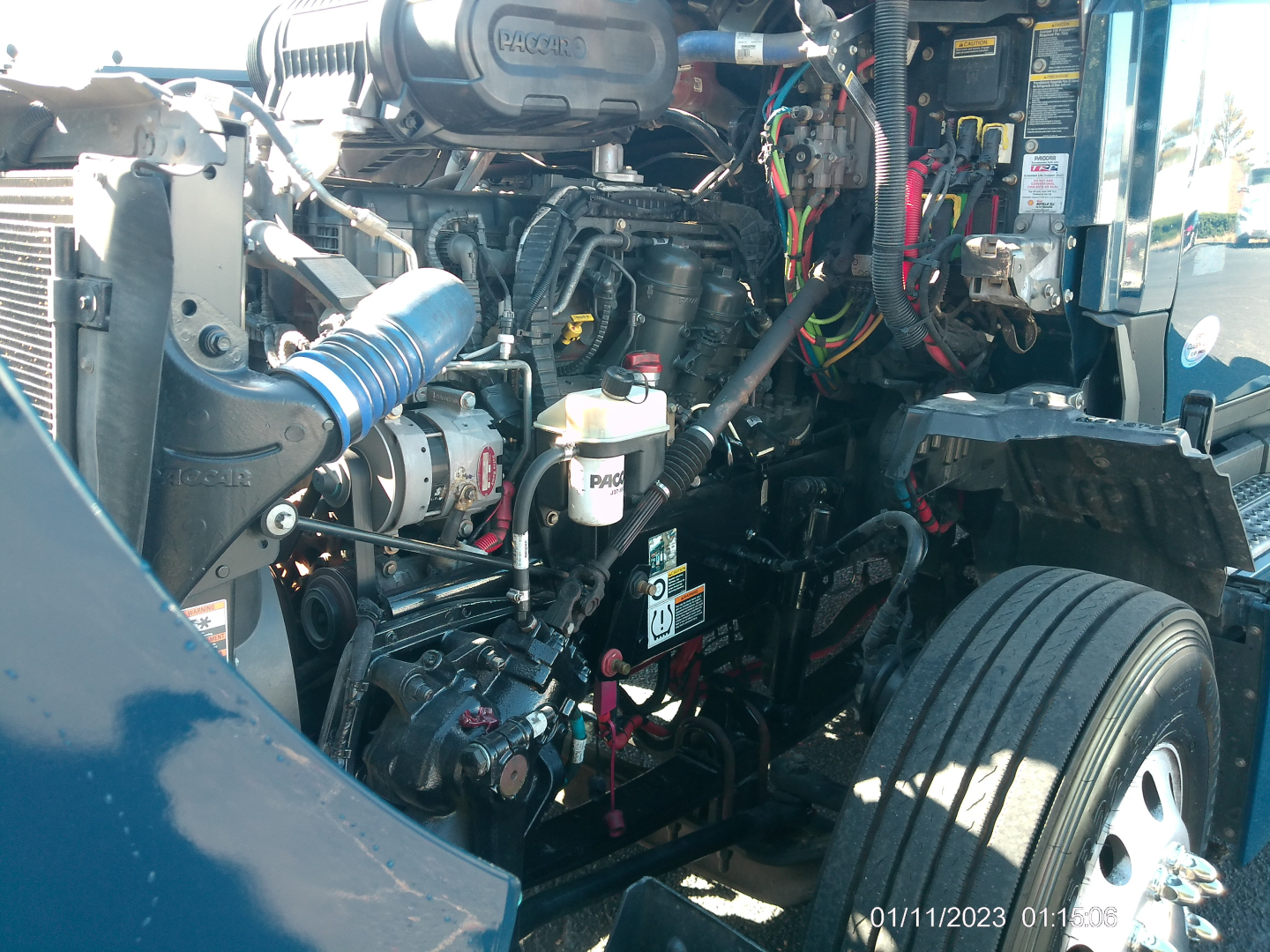 Kenworth T680 engine bay showing large engine with hoses, wires, and fluid reservoirs; visible labels and components in the bay.