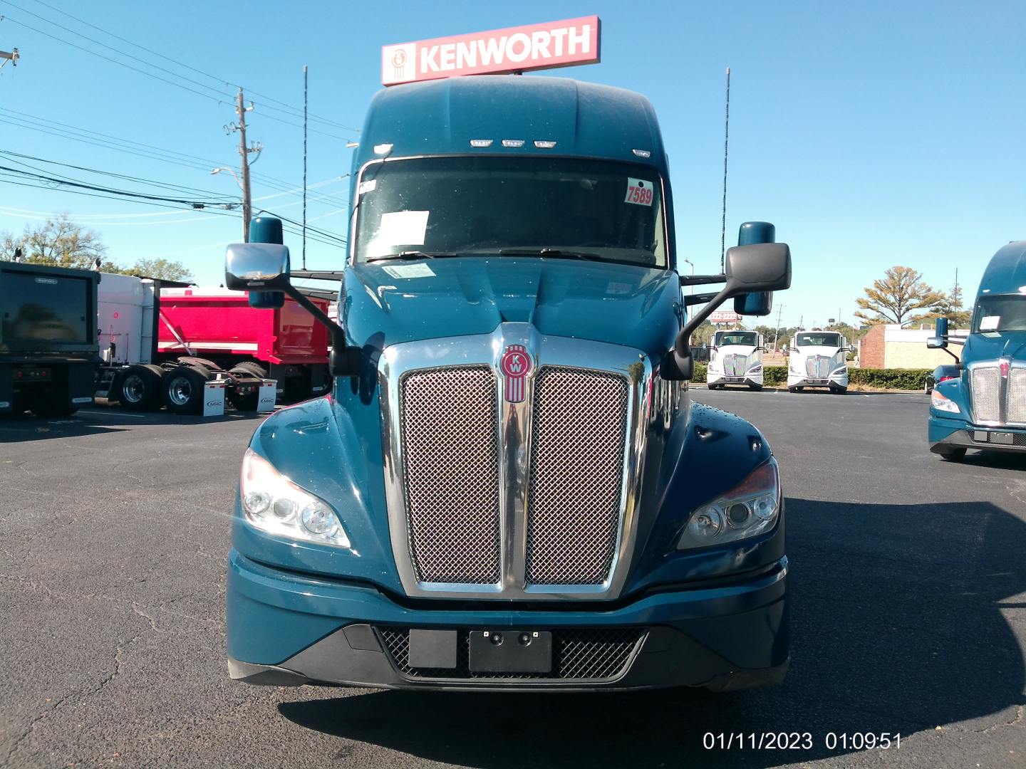 Kenworth T680 front view showing chrome grille and headlights in blue cab with Kenworth sign in background.