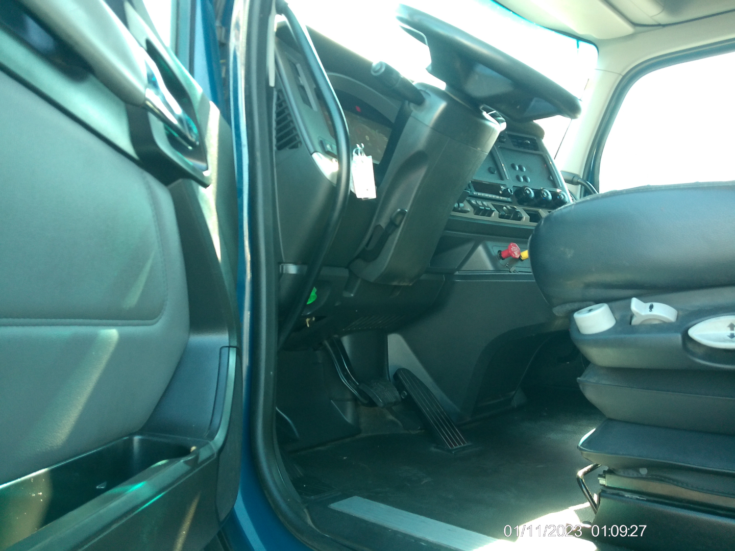 Kenworth T680 interior cabin view from driver door, showing steering wheel, dashboard, pedals, and seating area.