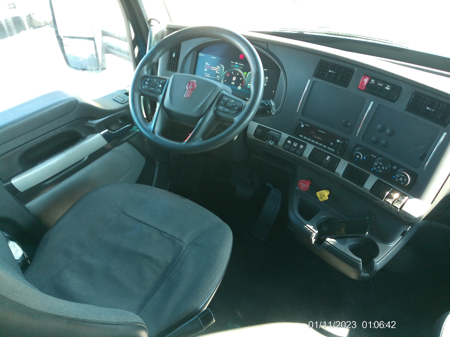 Kenworth T680 truck interior cockpit with steering wheel, dashboard, and control panels; visible gauges, buttons, and cup holder area.