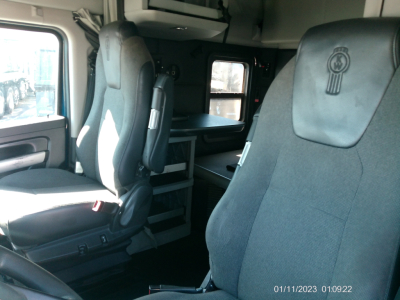 Kenworth T680 truck interior front seats and sleeper area, gray fabric seats with Kenworth emblem, cab with side window, dashboard area visible.