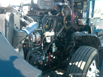 Kenworth T680 engine bay showing large engine with hoses, wires, and fluid reservoirs; visible labels and components in the bay.