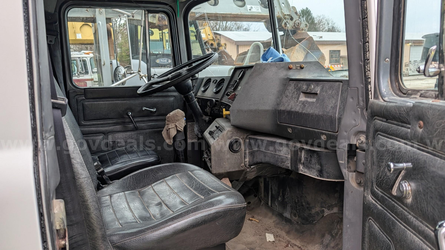 Mack RD690S cab interior showing steering wheel, dash, and black vinyl seat with dashboard cluttered area and doors open.