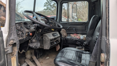 Cab interior of a 1994 Mack RD690S dump truck showing steering wheel, dashboard gauges, driver seat, and worn flooring