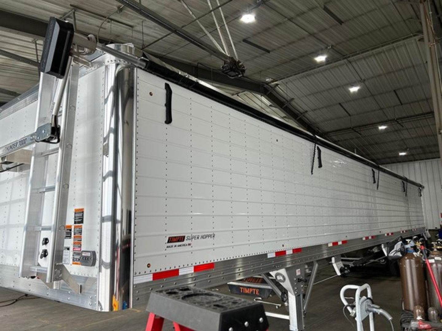 Timpte Super Hopper trailer side view showing aluminum panel walls and storage features with brand label visible.