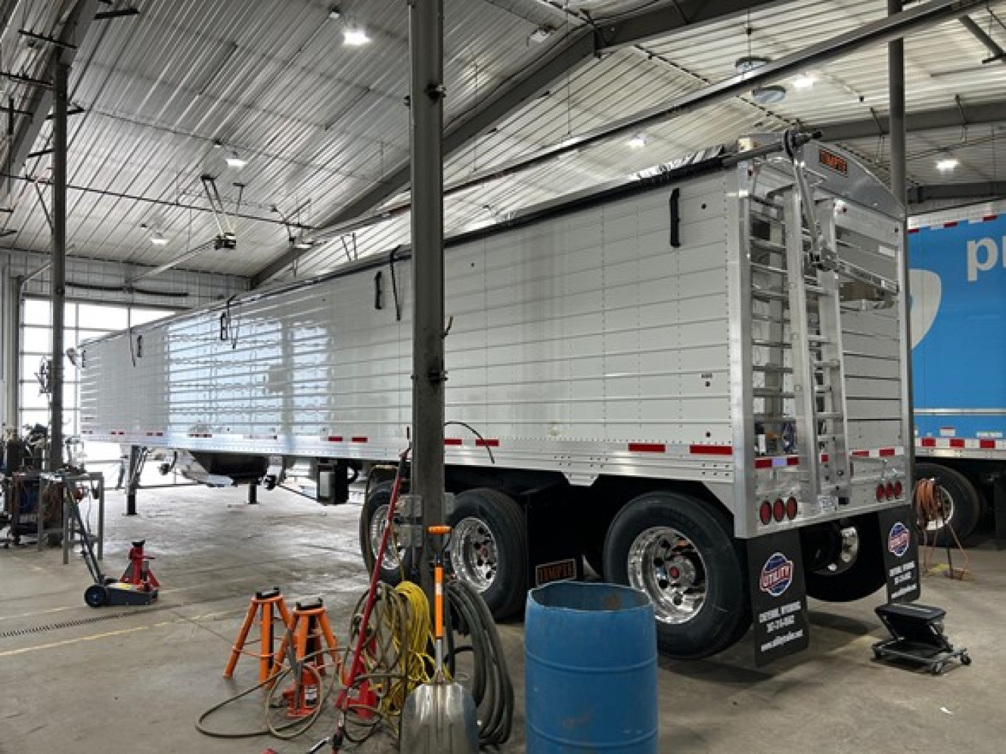 Trailer side view showing a white Timpte Super Hopper trailer with dual rear doors and aluminum sides in a workshop.