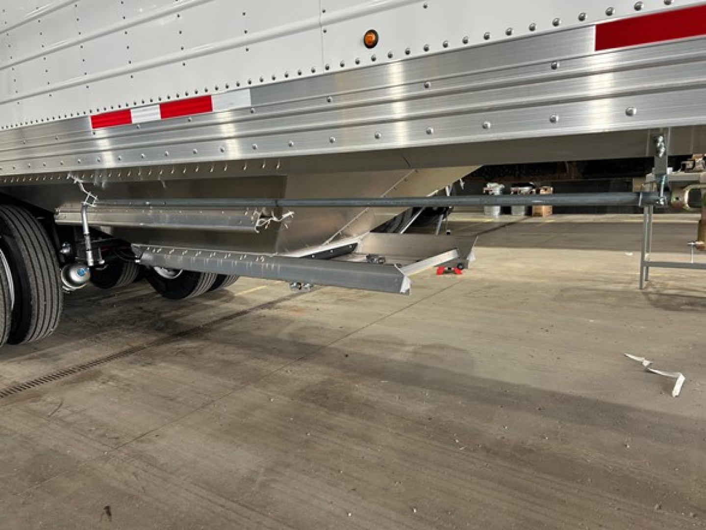 Trailer undercarriage with supporting beam and landing gear, side of a Timpte Super Hopper trailer showing silver painted components and reflective tape.