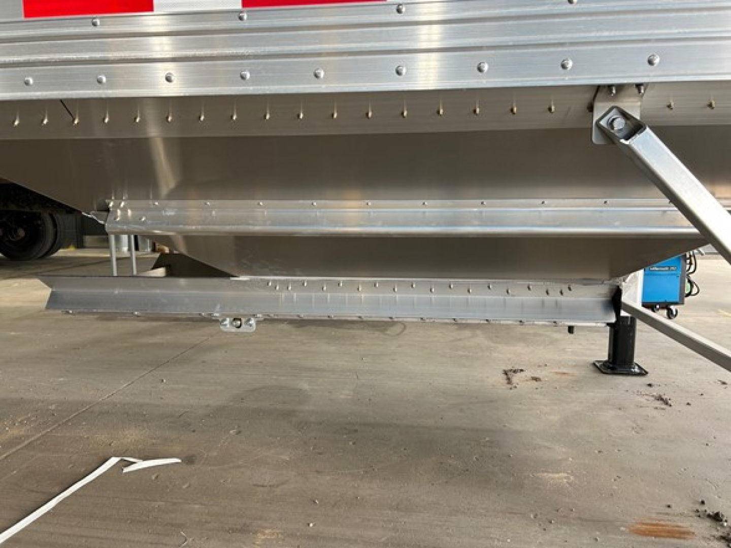 Timpte Super Hopper trailer side view showing underside frame and landing gear with riveted aluminum panels and support braces.