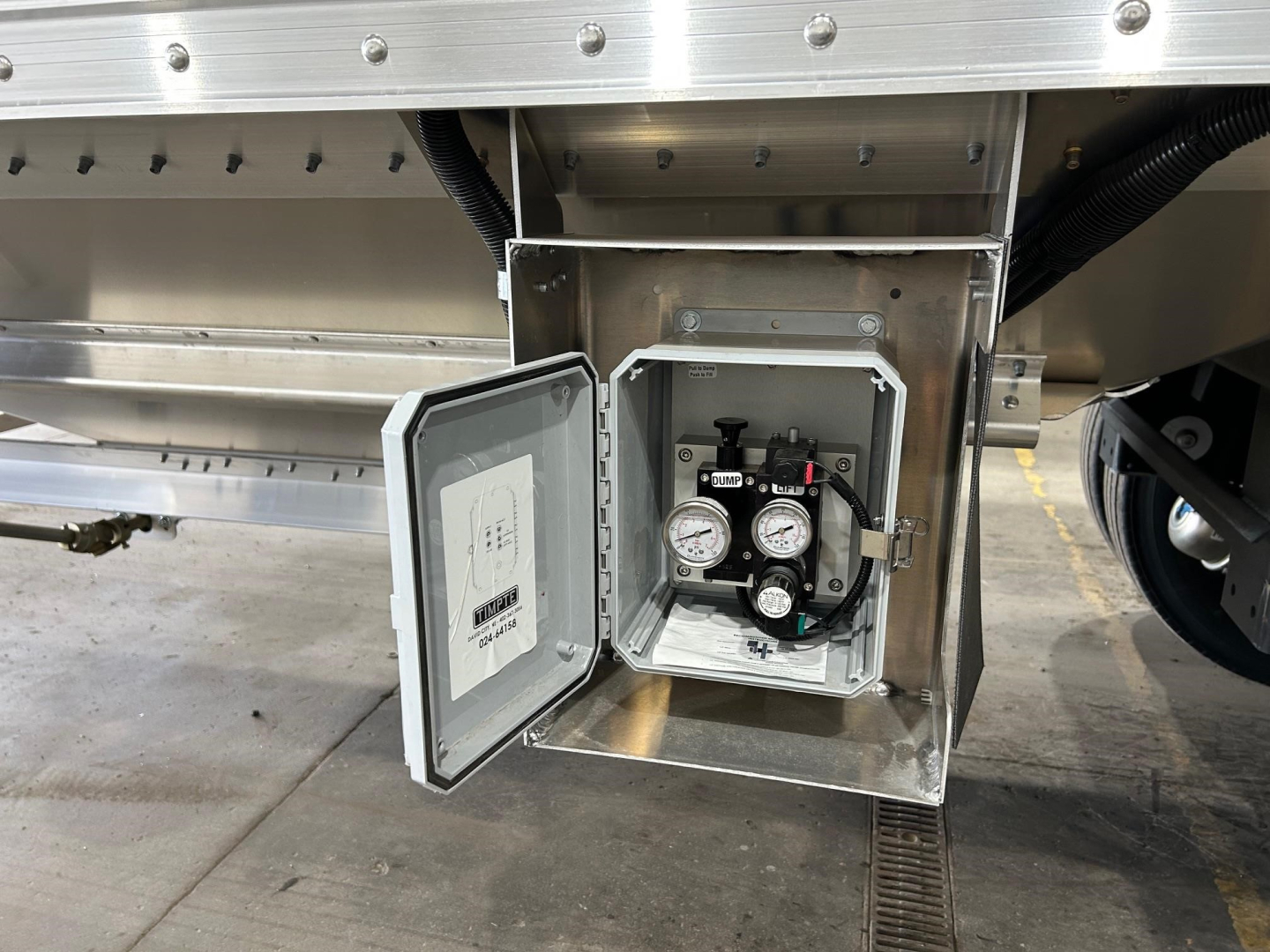 Trailer valve box open showing pressure gauges and control valves mounted inside a metal cabinet on a Timpte Super Hopper trailer.