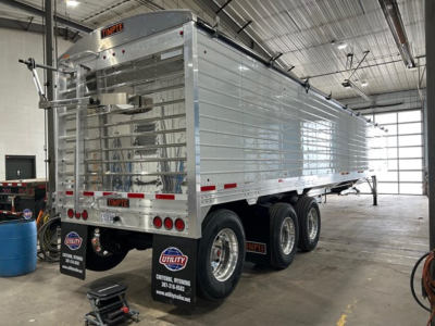 Timpte Super Hopper trailer in a workshop, rear and side view showing dual rear doors, triple axle wheels, reflective tape, and utility branding.