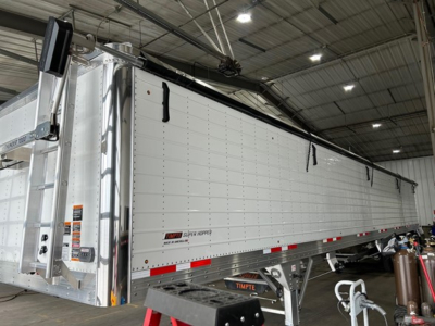 Timpte Super Hopper trailer side view showing aluminum panel walls and storage features with brand label visible.
