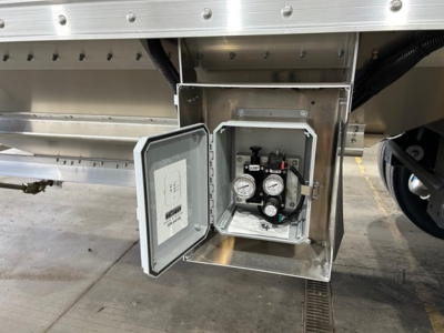 Trailer valve box with pressure gauges and control manifold mounted on side of new Timpte Super Hopper trailer. Shows open rectangular enclosure with gauges and piping inside.
