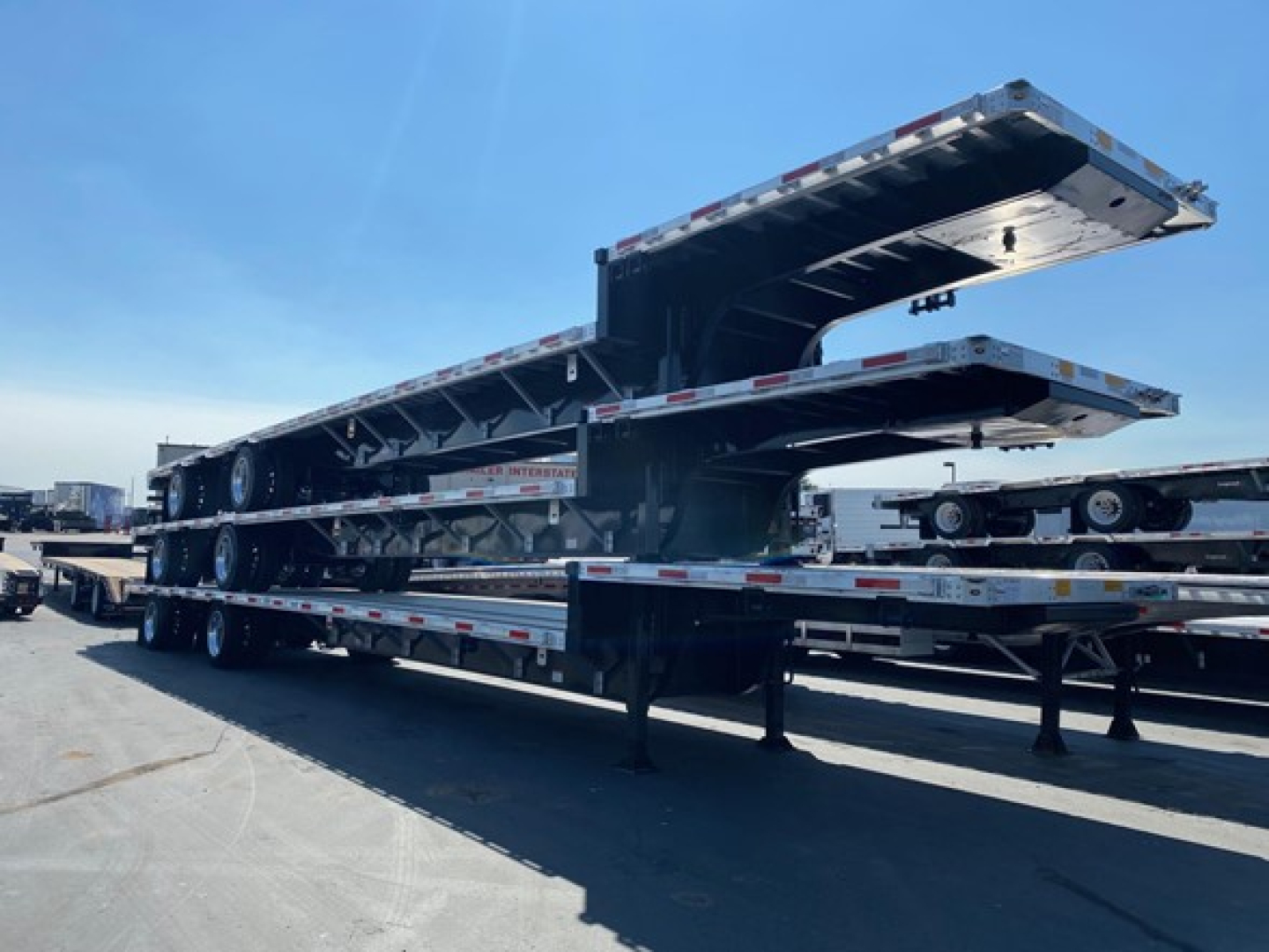 Trailer deck with drop-down sections in up position showing multiple axles and reflective safety tape.