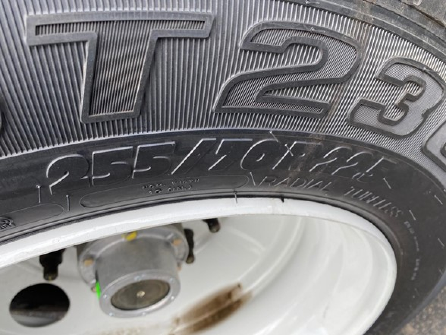 Truck tire with visible tread and wheel hub; close-up shows tire markings including 'T123' style characters and wheel hub details.