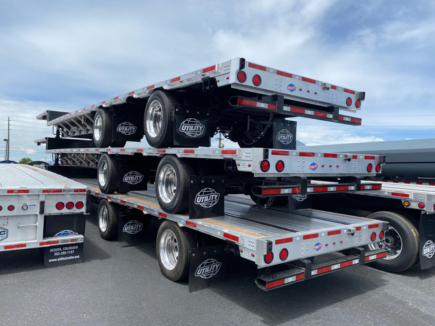Utility Cal Legal Combo Drop Deck trailer stacked with three trailers in a lot; visible wheels, mud flaps with Utility logo, reflective tape along frame.