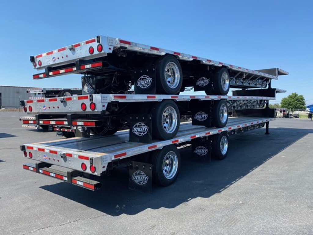 Triple-stack flatbed trailer combination on a tri-axle drop deck with Utility HWT branding and spare tires visible.