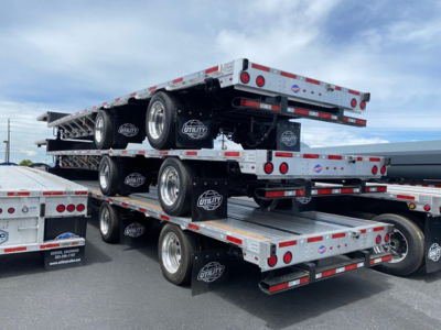 Trailer stack showing multiple Utility drop deck trailers with black wheels and branding, stacked on top of each other in a lot.
