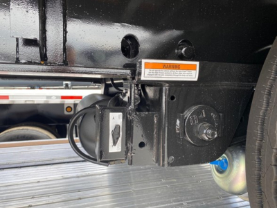 Utility trailer hitch area showing a circular 7-pin connector and a small electric control plug, warning sticker, and steel frame.