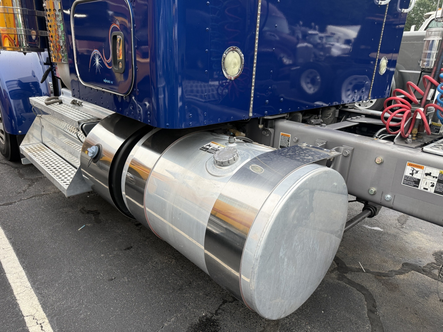 Kenworth W900L fuel tank mounted under blue truck cab with side steps and chrome tank; cylindrical aluminum fuel tank with cap and straps visible.
