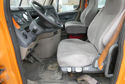Truck cab interior showing steering wheel, gray fabric seats, and dashboard in a Freightliner Cascadia 125 daycab.